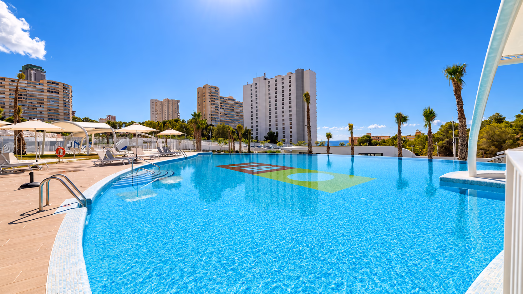 Outdoor pool with sun loungers under parasols and the Poniente towers behind