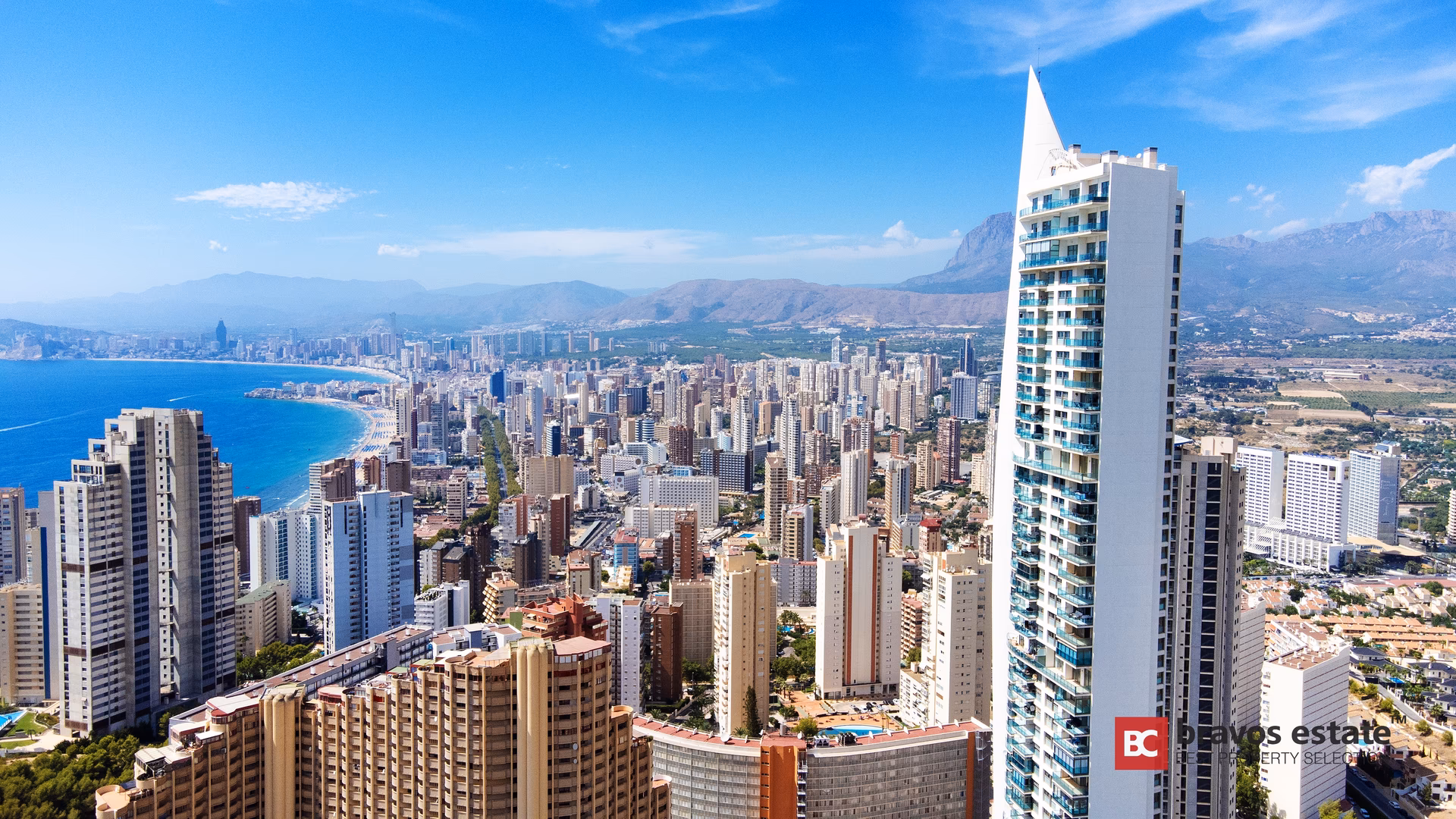 Torre Lugano — белая башня со шпилем над Бенидормом; за ней пляж Леванте, небоскрёбы города и горы